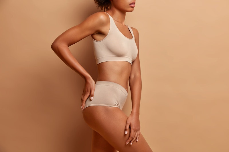 Side profile of woman wearing beige underwear with hands on hip and thigh