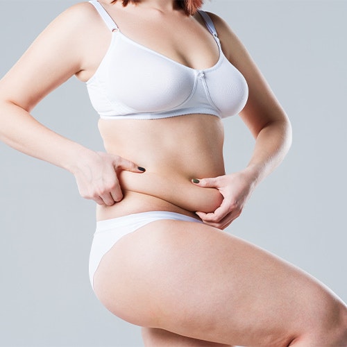 a woman pinching her belly fat and considering a tummy tuck