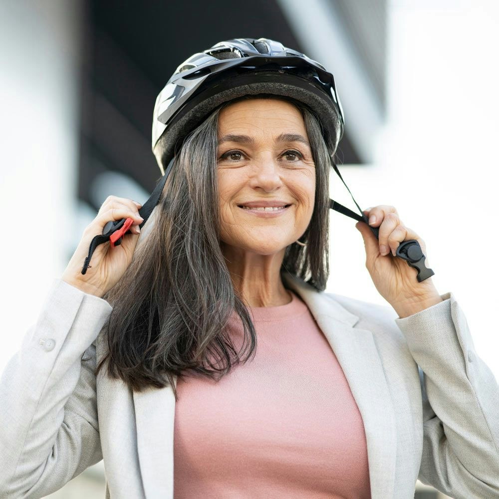 Woman putting on bike helmet while wearing a pink shirt outdoors