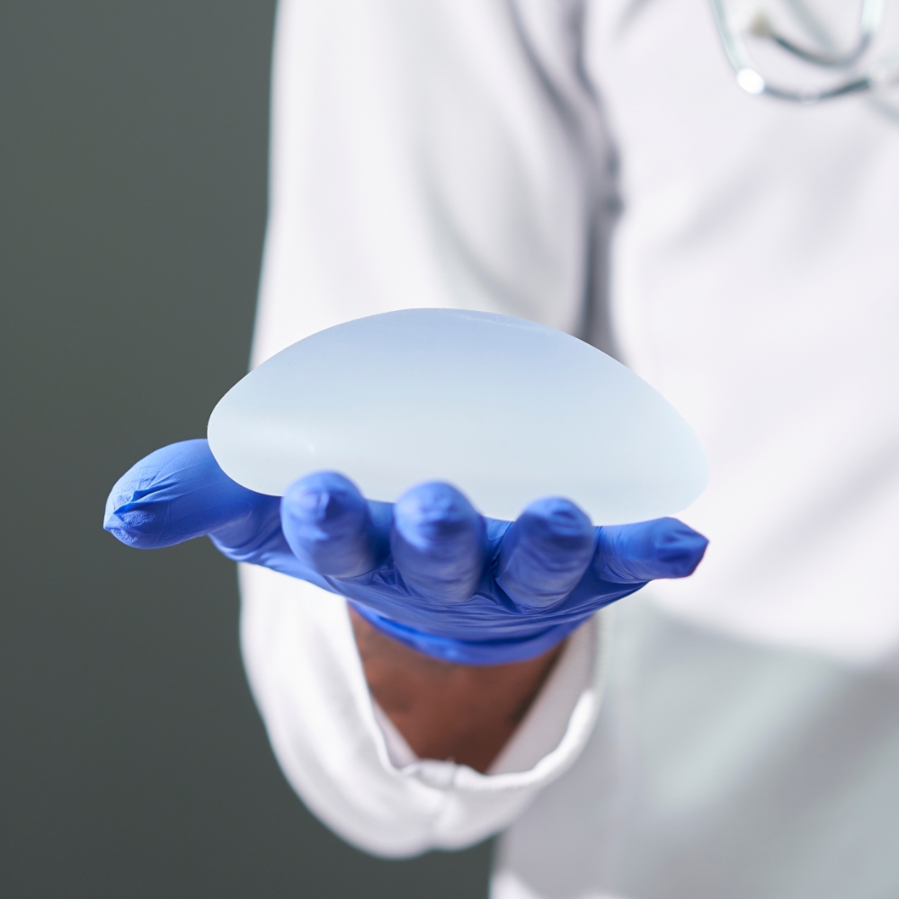 A doctor's gloved hand holding a breast implant