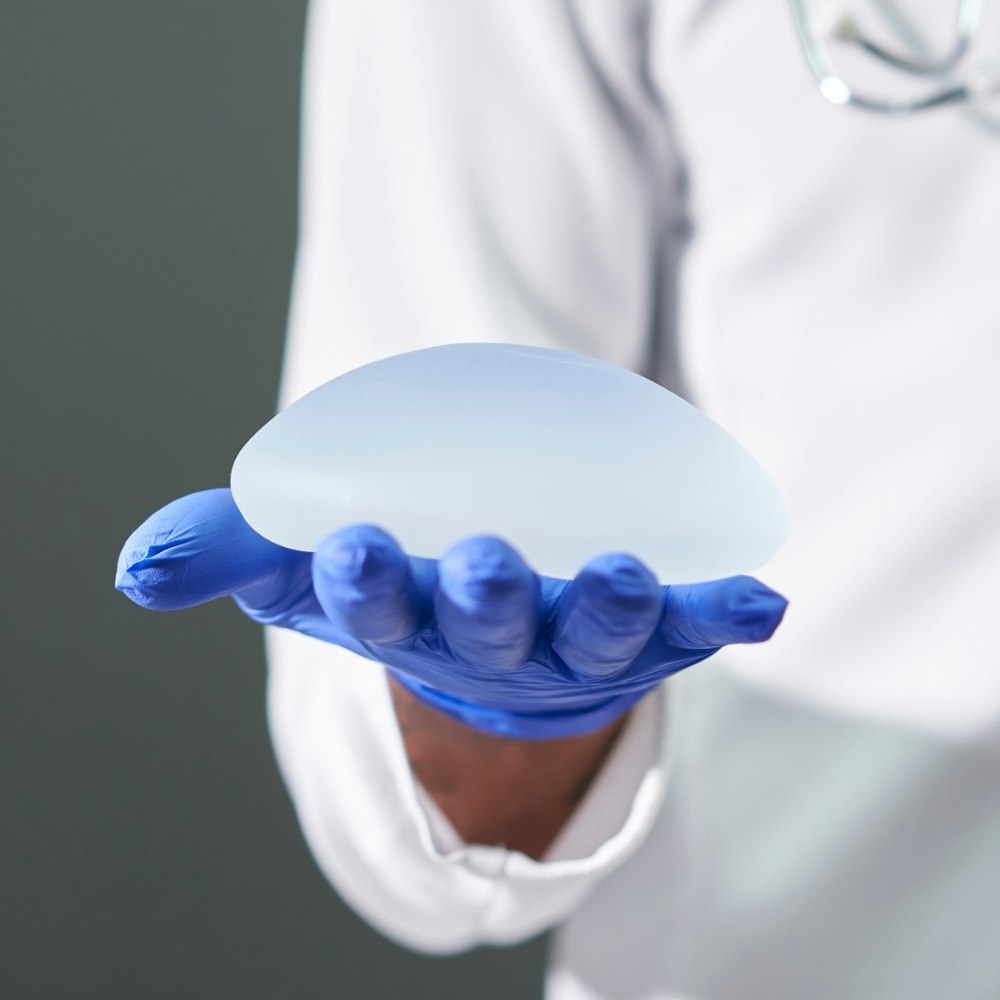 A doctor's gloved hand holding a breast implant