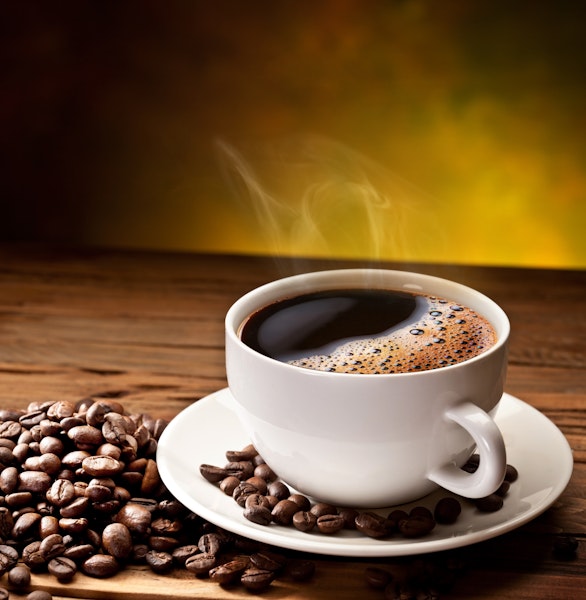 steaming cup of black coffee surrounded by coffee beans