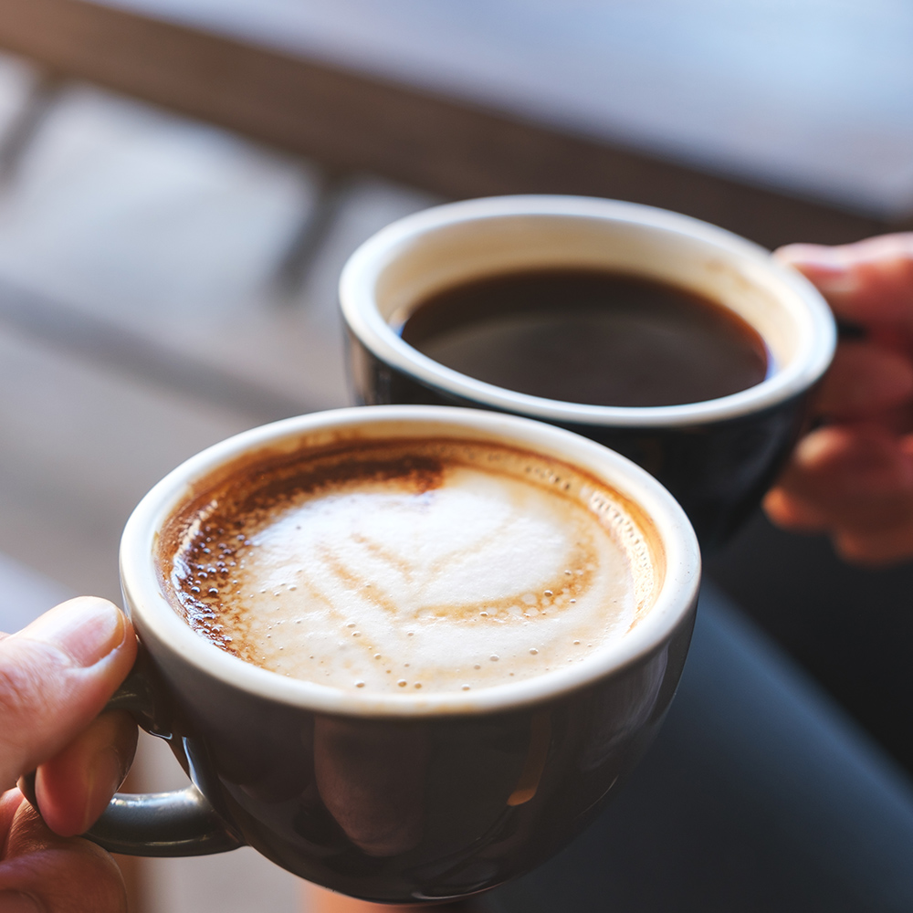 steaming cup of black coffee surrounded by coffee beans
