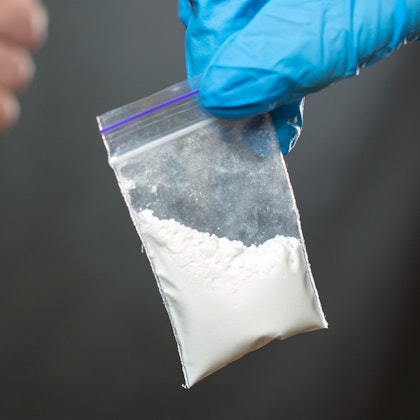 Drugs in plastic bag held by someone wearing blue gloves