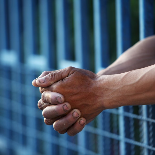 Close-up of hands sticking out from jail bars