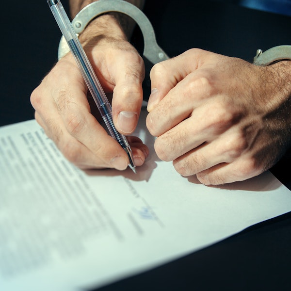 Person in handcuffs signing documents