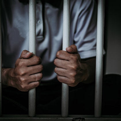 Close up of hands grabbing bars from inside a jail cell