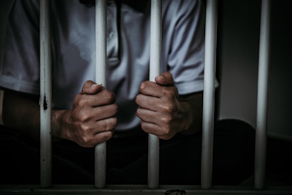 Close up of hands grabbing bars from inside a jail cell