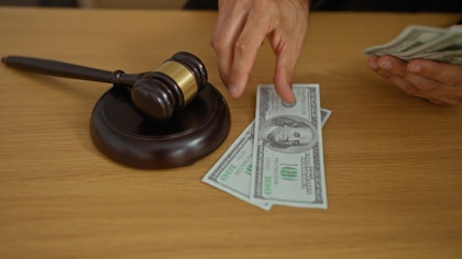Hands placing U.S. hundred dollar bills down by a gavel