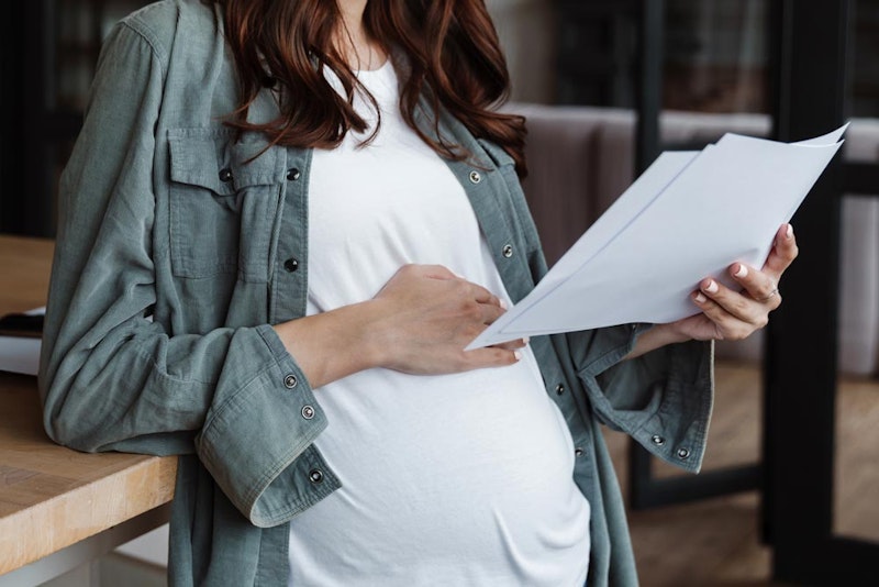 Pregnant woman touching belly while reading through documents