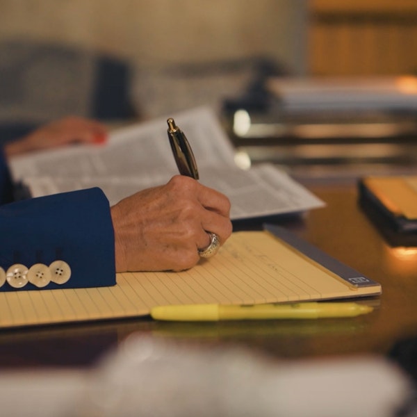 Close-up of Debra J. Sutton writing notes on a legal pad with an open book nearby