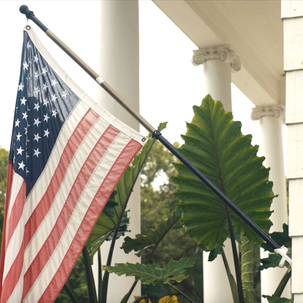 American flag displayed on a front porch with white columns and large green foliage