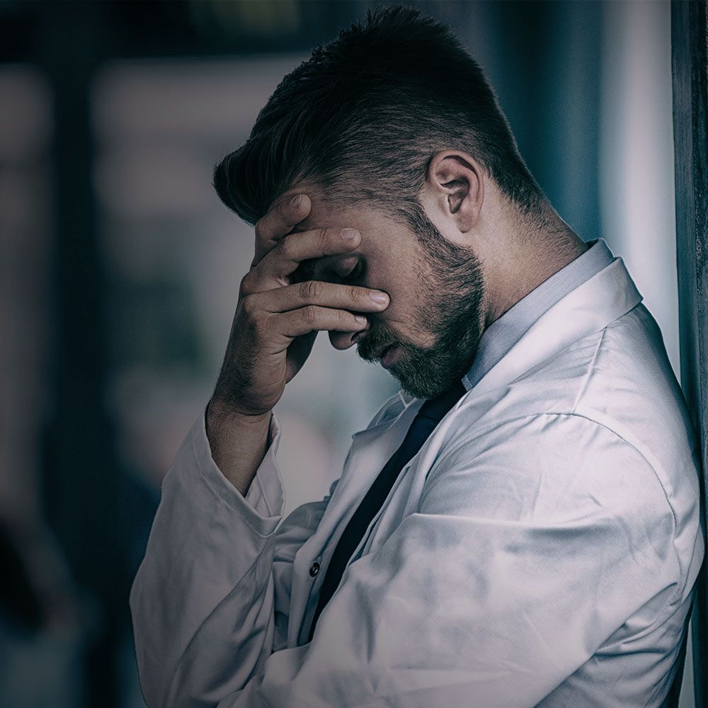 doctor with his head down and his hand on his forehead