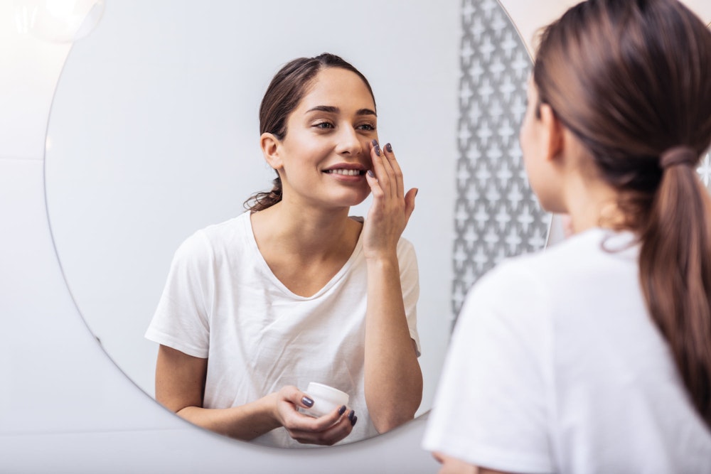 woman putting on moisturizer in the mirror