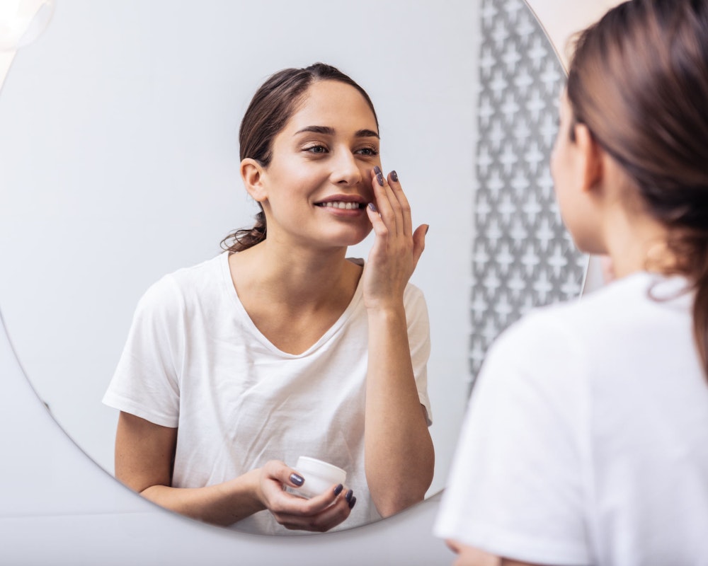 woman putting on moisturizer in the mirror