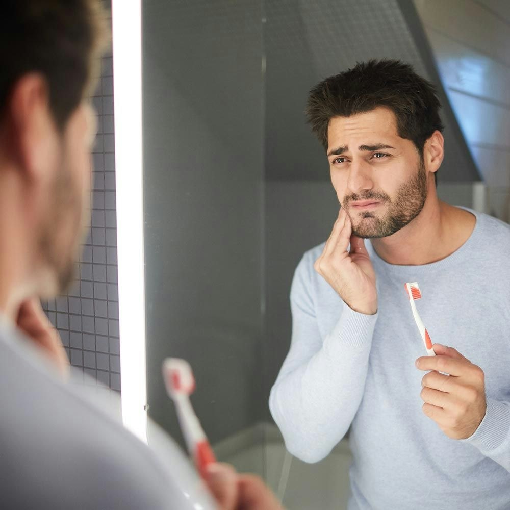 Man holding jaw in pain while brushing teeth