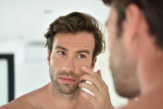 Man considering BOTOX touching face and looking in the mirror