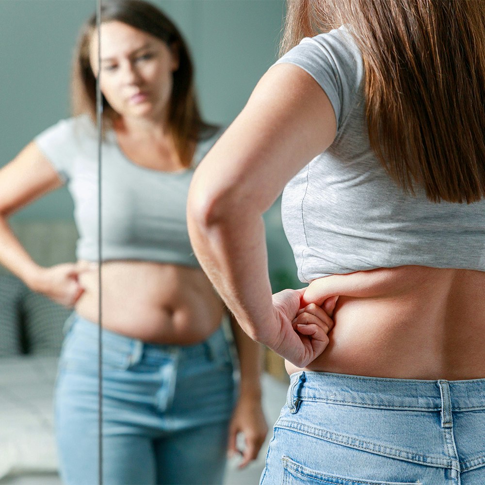 a woman assessing her body in a mirror