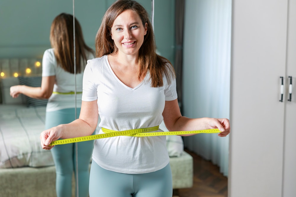 Woman smiling while measuring her waist