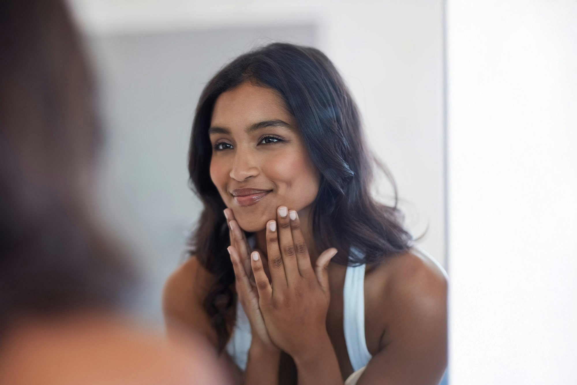 Beautiful smiling woman looking in the mirror after injectables treatment