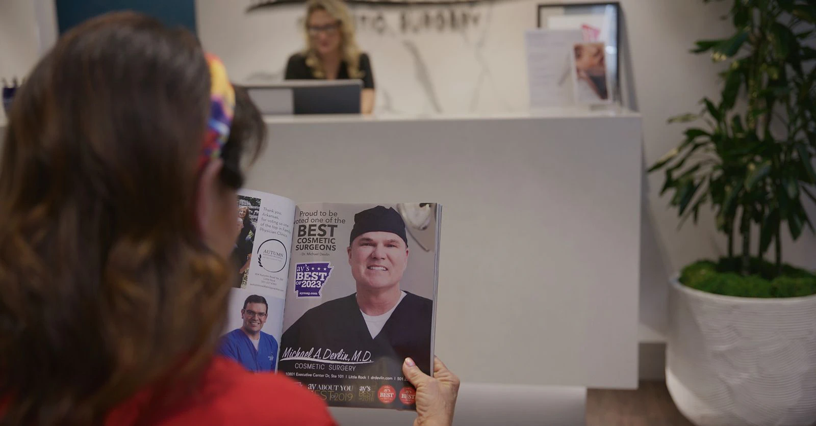 A patient at the Devlin Cosmetic Surgery front desk holds an AY Magazine issue featuring Dr. Devlin as Best Cosmetic Surgeon
