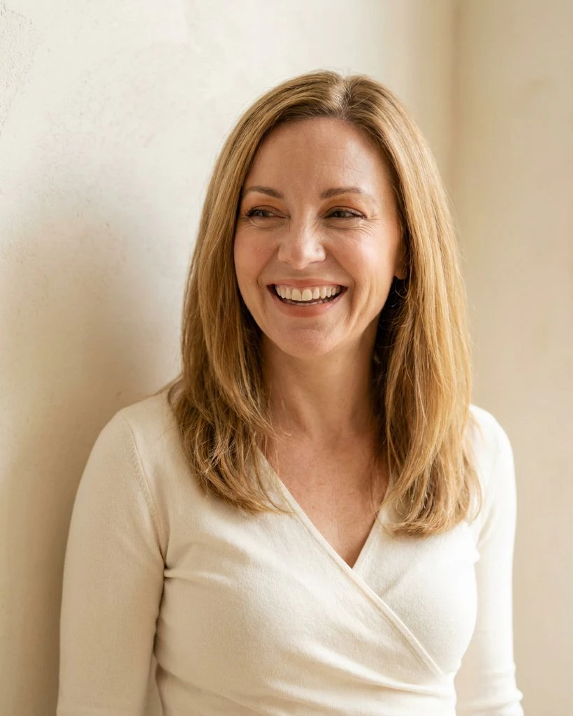 A laughing woman with honey-blonde hair in an ivory wrap top