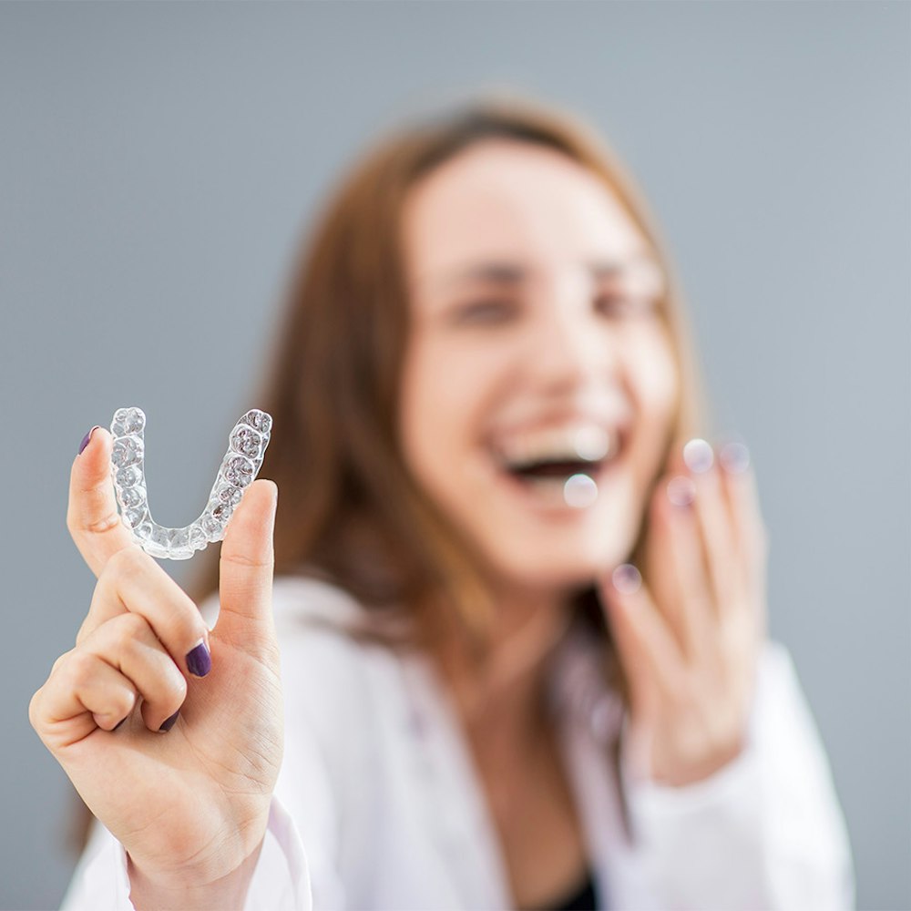 Girl smiling while holding an invisalign aligner