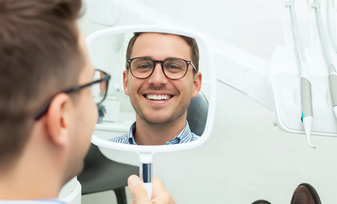 Man smiling in a handheld mirror at the dentist
