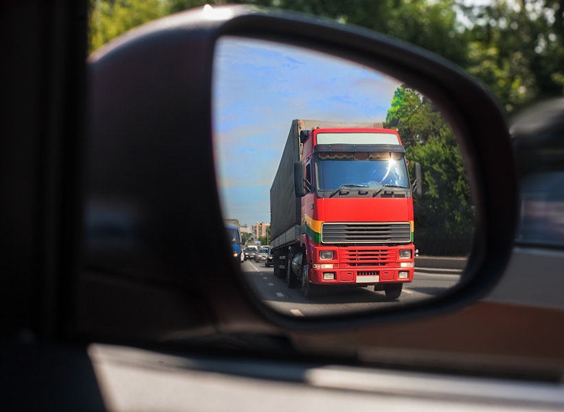 red 16-wheel truck shown in a car's side mirror
