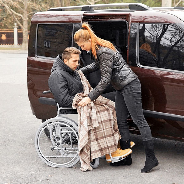 woman helping man in wheelchair into a car