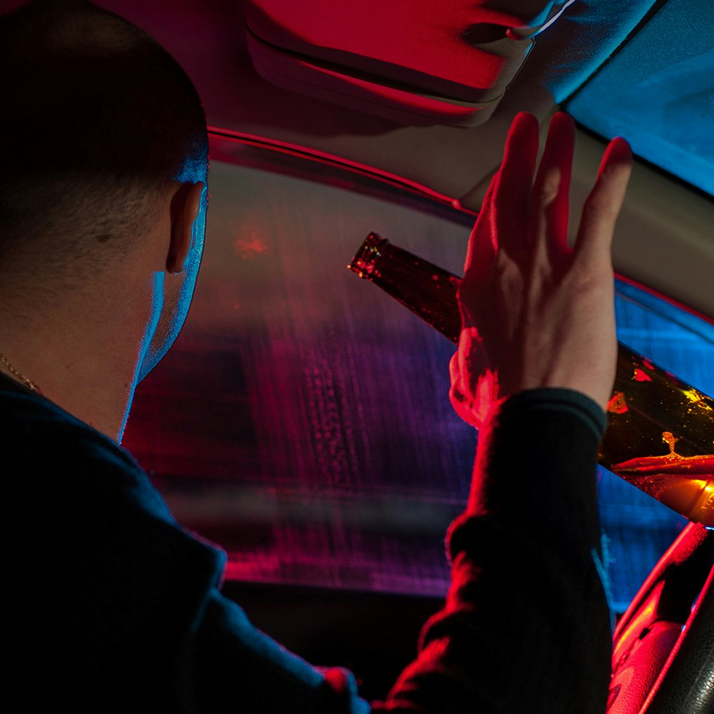 Hand holding beer bottle next to gear shift of car