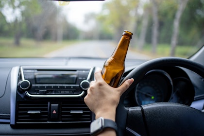 Person holding alcohol bottle while driving