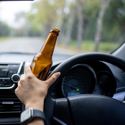Person holding alcohol bottle while driving