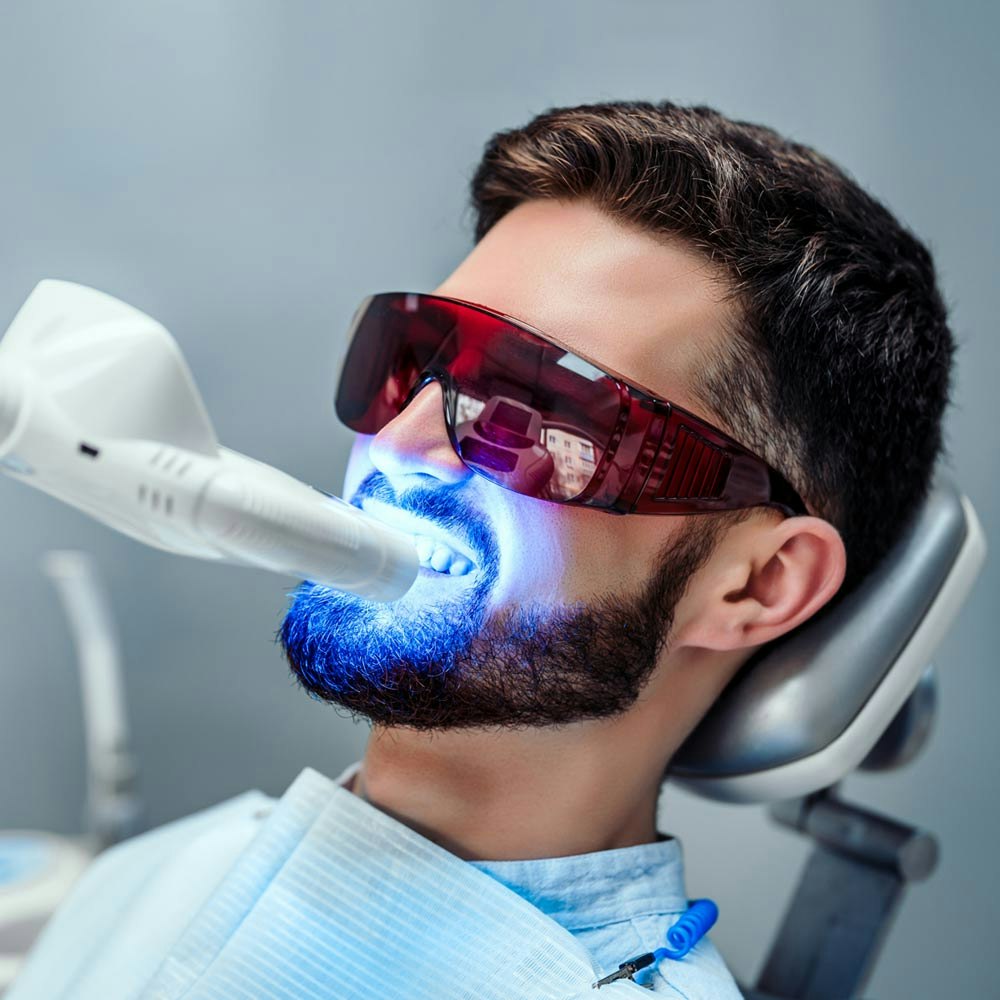 Bearded man in dental chair receiving teeth whitening treatment
