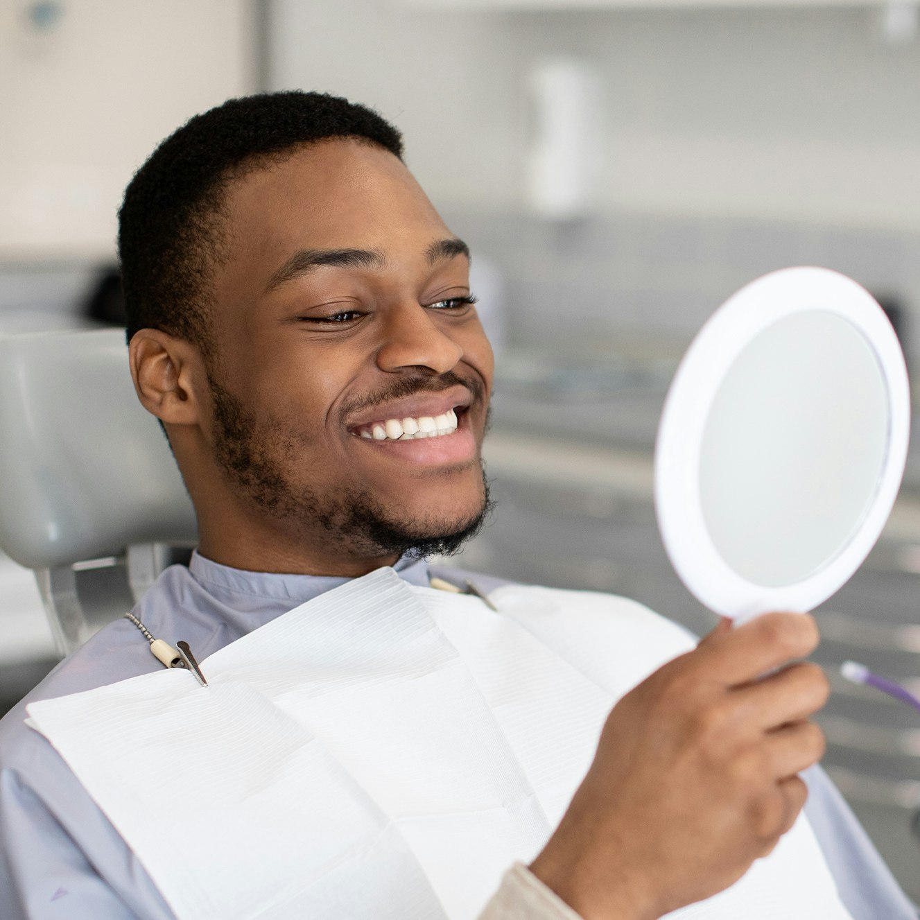 Dental patient looking at new smile with hand mirror