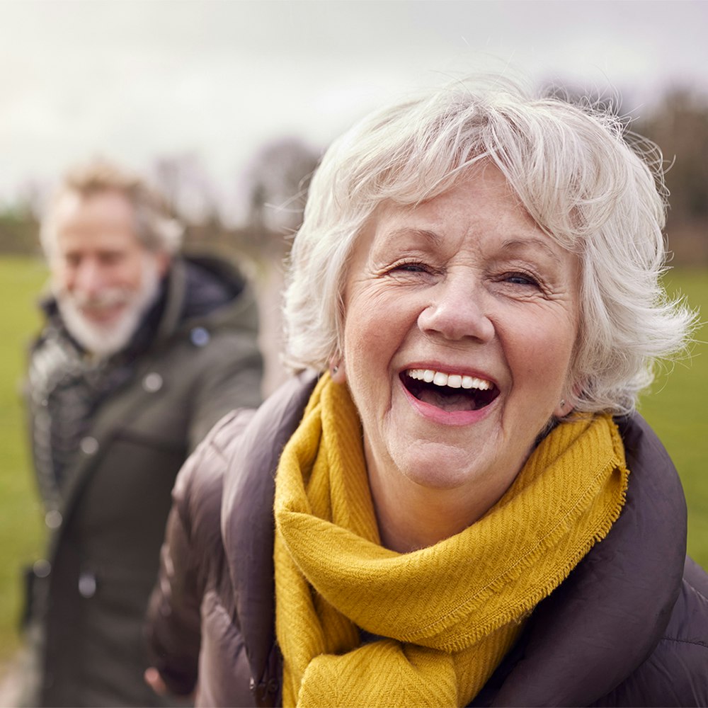 Older couple with dental crowns smiling while holding hands outside