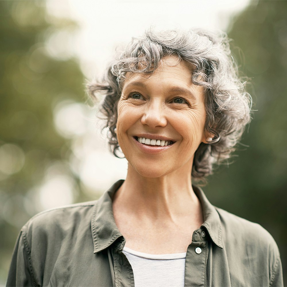 Older woman with dental implants smiling in a park