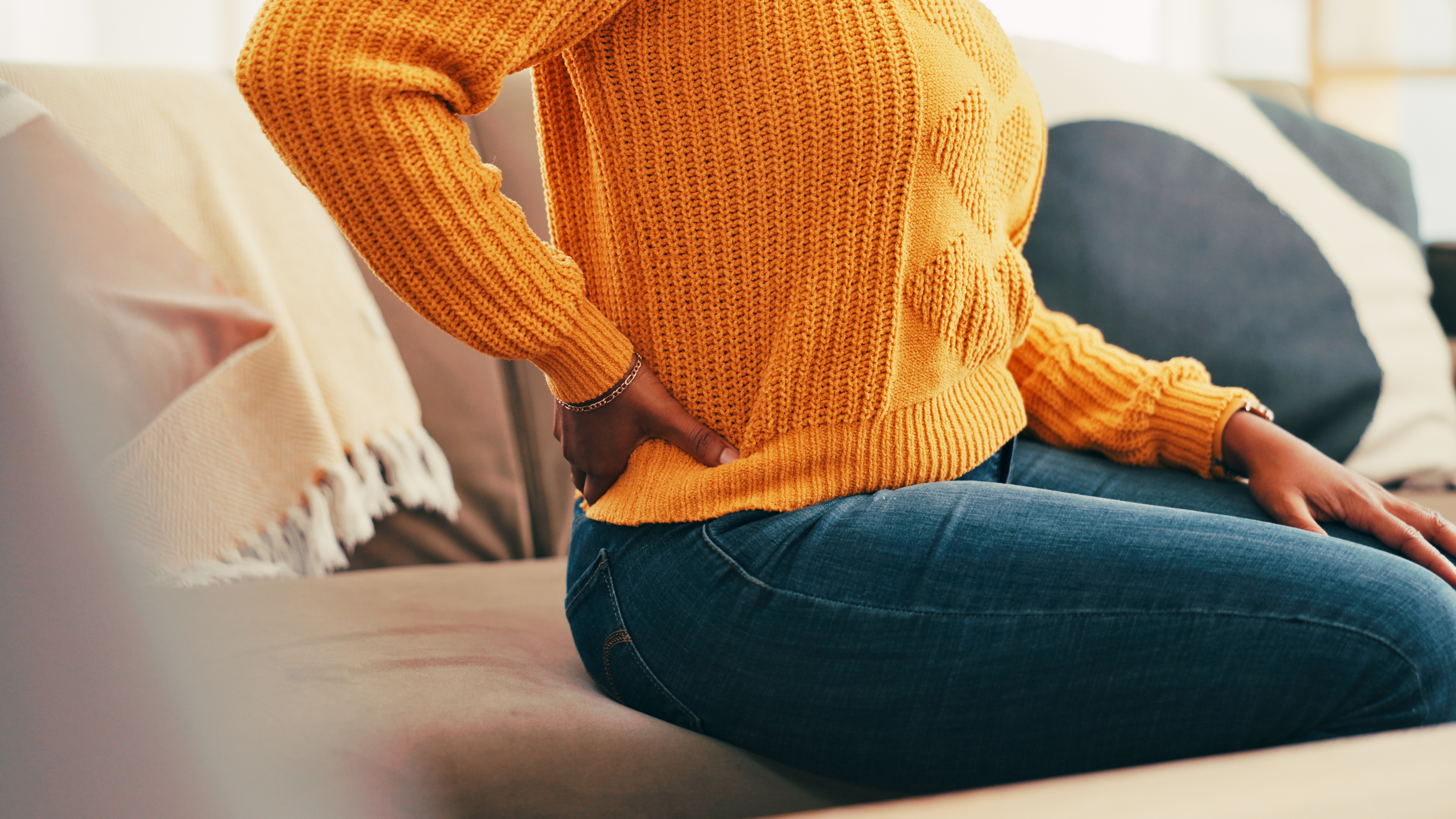 woman in orange sweater holding lower back in pain