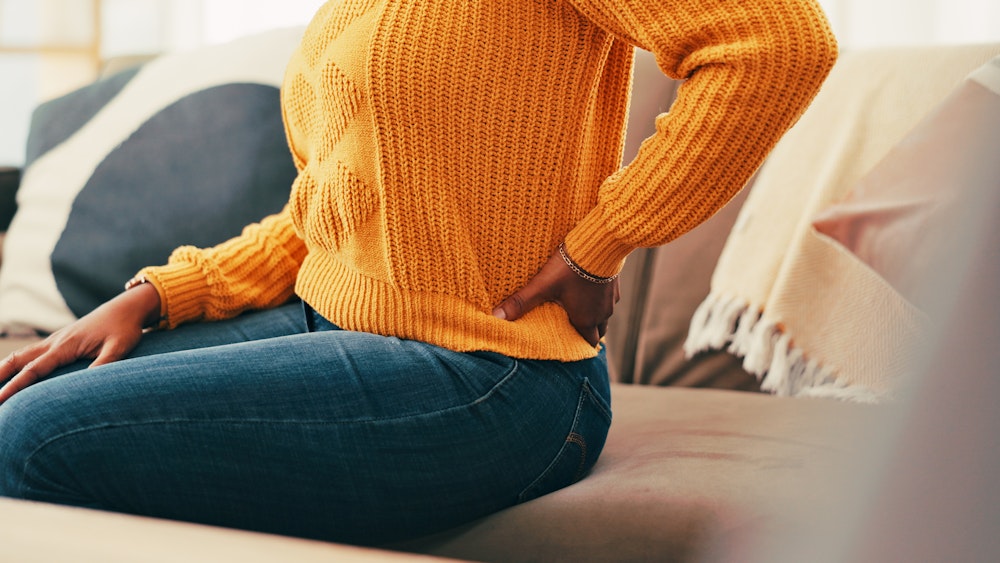 woman in orange sweater holding lower back in pain