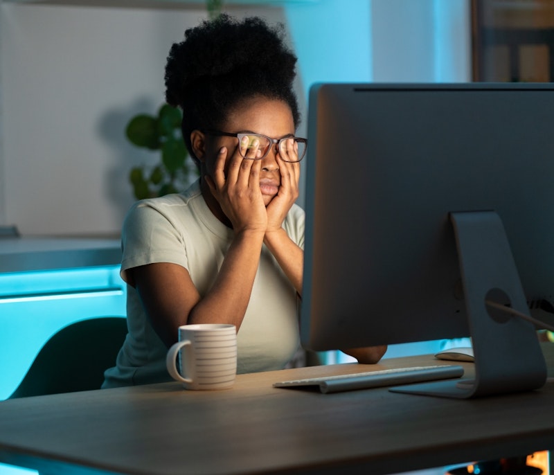 woman rubbing eyes in front of the computer