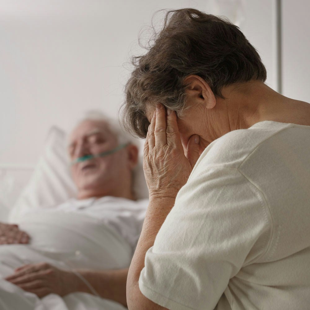Mature woman mourning with loved one in hospital bed