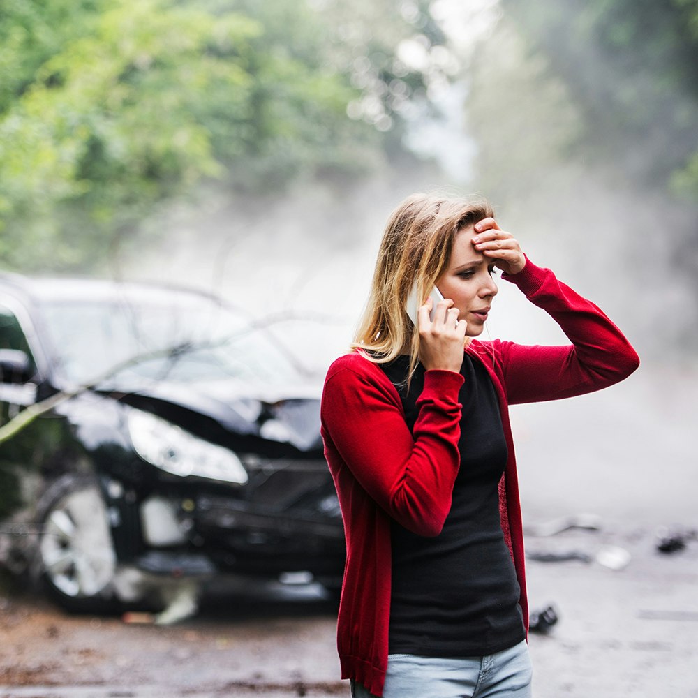 a woman on her cell phone with a wrecked vehicle in the background