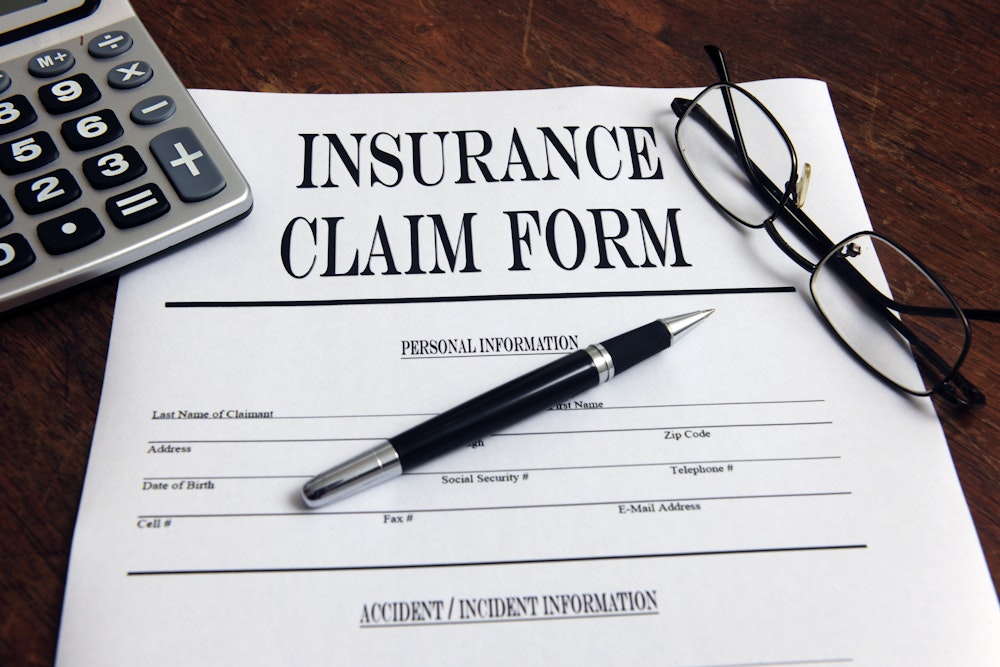 Rejected insurance claim form, pen, glasses and calculator