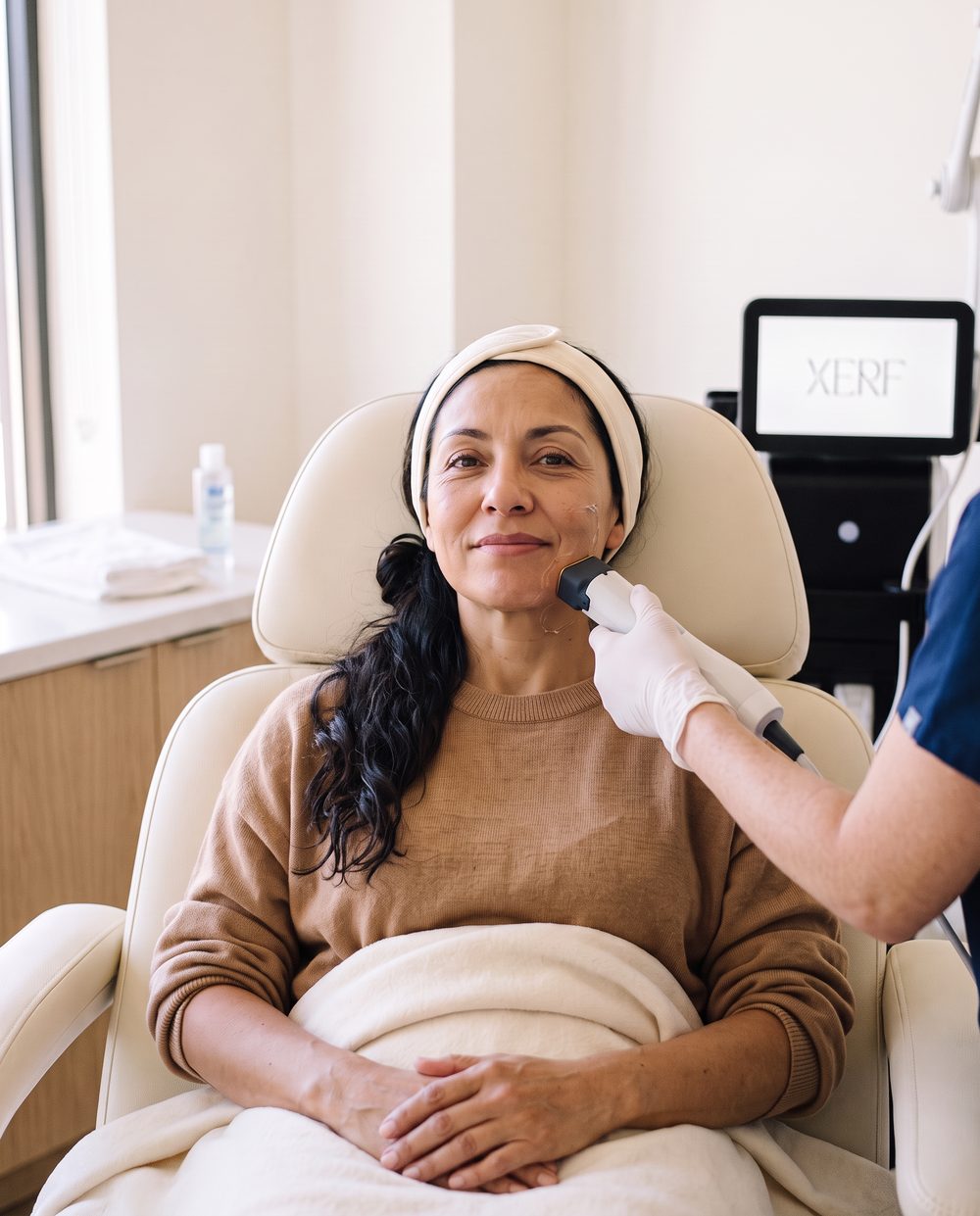 A woman relaxes in a treatment chair as the XERF handpiece glides along her lower cheek