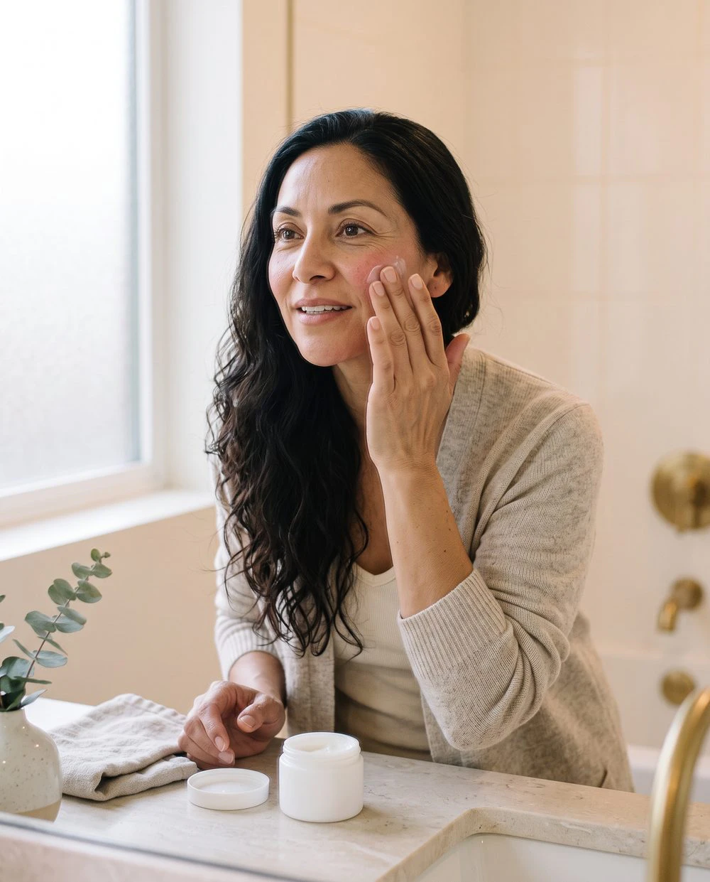 A woman smooths moisturizer onto her cheek at home after treatment
