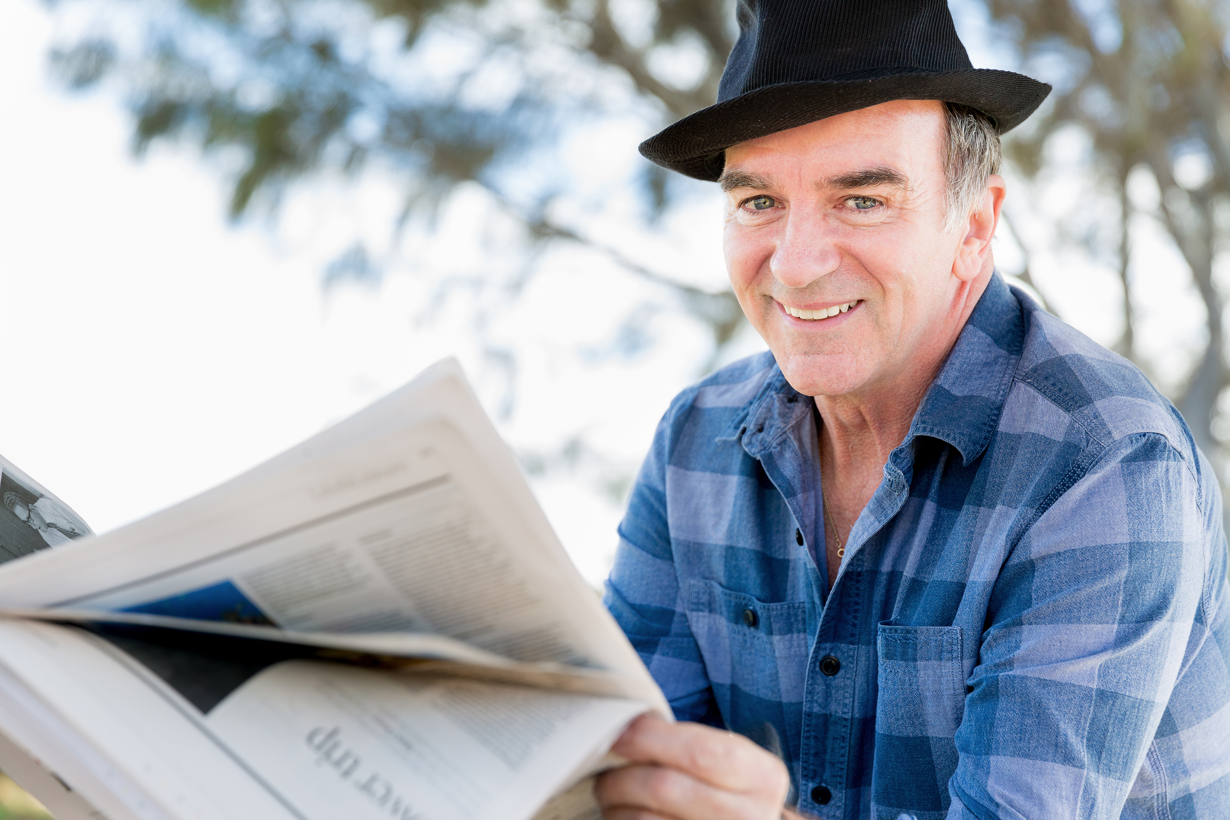 Smiling older man in hat reading outdoors