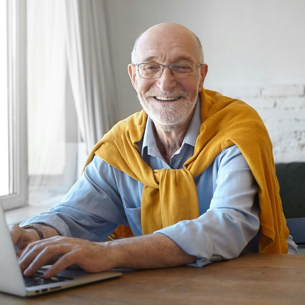 Older man at laptop with sweater over shoulders