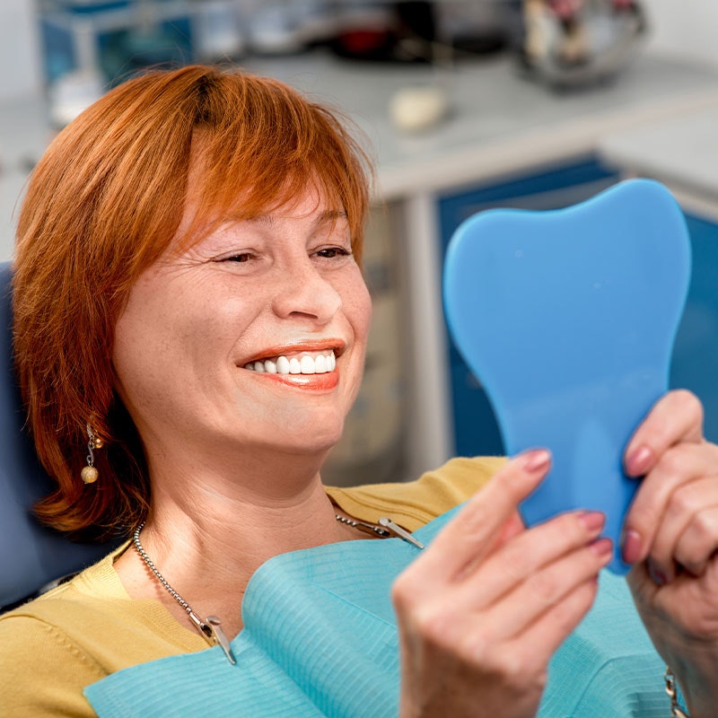 Smiling woman with dentures looking in the mirror at the dentist