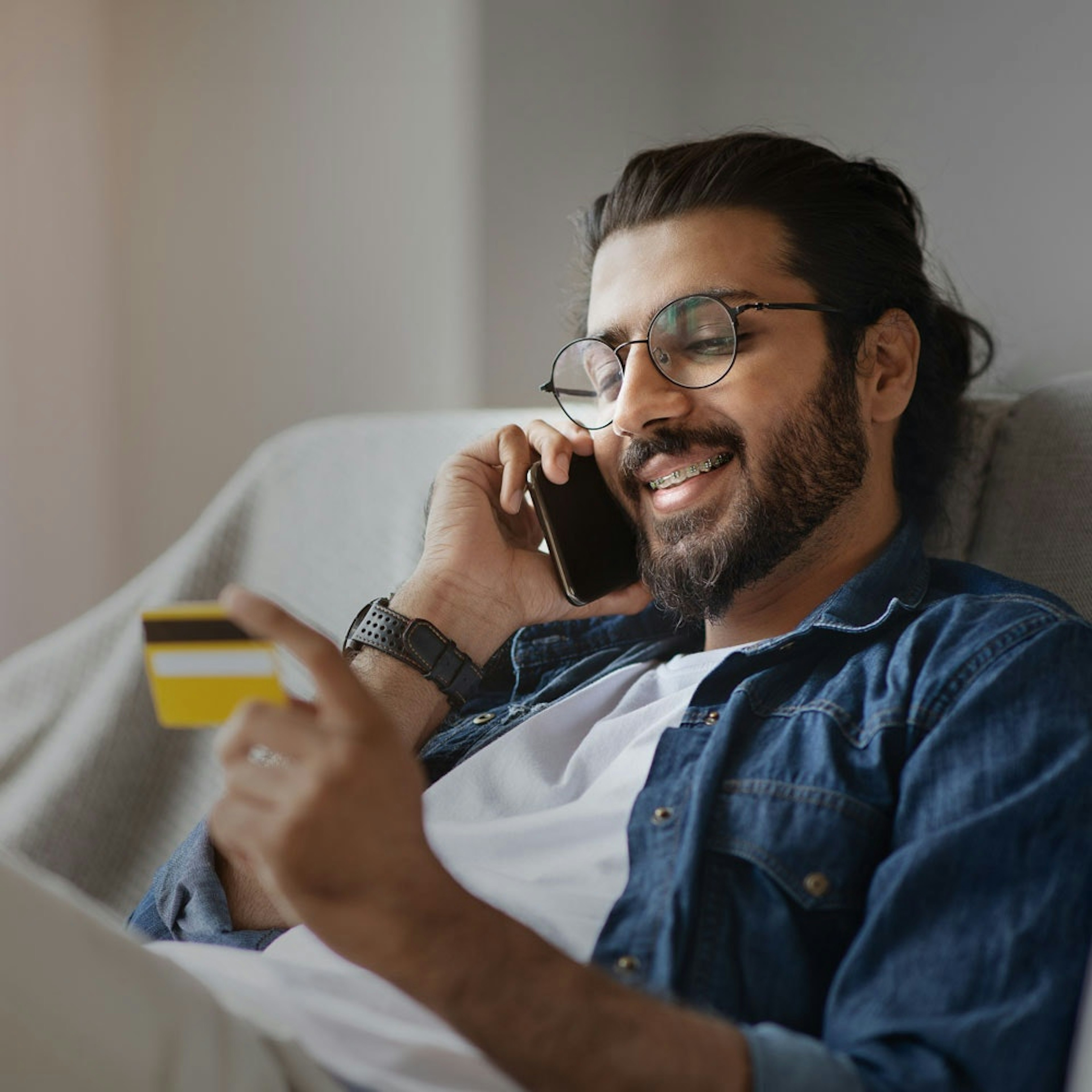 Smiling man wearing braces on the phone holding credit card