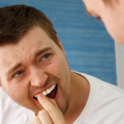 man suffering from gum disease wiggling tooth in mirror